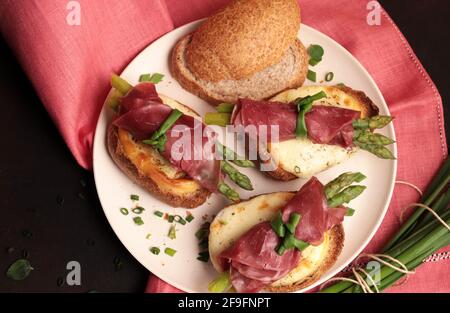 Bresaola und Spargelbrötchen mit Käse und geröstetem Brot auf dunklem Hintergrund. Gesunde Ernährung. Blick von oben. Stockfoto