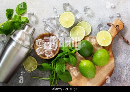 Erfrischende kalte Sommer Mojito Cocktail Herstellung. Minze, Limette, Eiszutaten und Barutensilien auf einem Stein- oder Betontisch. Draufsicht flach liegend. Stockfoto