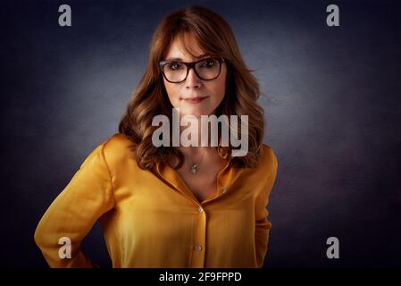 Studioportrait einer attraktiven Frau mittleren Alters, die auf einem isolierten dunklen Hintergrund steht. Speicherplatz kopieren. Stockfoto