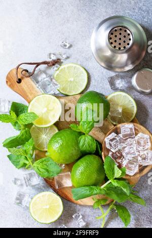 Erfrischende kalte Sommer Mojito Cocktail Herstellung. Minze, Limette, Eiszutaten und Barutensilien auf einem Stein- oder Betontisch. Draufsicht flach liegend. Stockfoto