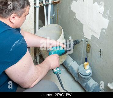 Reparatur-, Bau- und DIY-Konzept - Nahaufnahme eines Mannes mit einem elektrischen Bohrer, der ein Loch in die Wand macht. Stockfoto