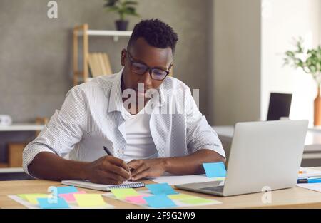 Junge gutaussehende gesinnte schwarze Geschäftsmann aufschreiben Ideen in Notebook Stockfoto