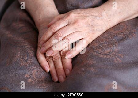 Faltige Hände einer älteren Frau, die mit einem Kopftuch bedeckt in ihrem Schoß gefaltet ist. Das Leben alter Menschen Stockfoto