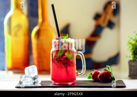 Frisch gepresster Erdbeersaft auf einem schwarzen Ständer und drei Orangen daneben Stockfoto