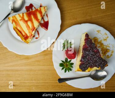 Set von Käsekuchen mit Erdbeer, Erdbeersoße, zerbröckeltem Gebäck und zwei Löffeln auf Holzboden. Draufsicht Stockfoto