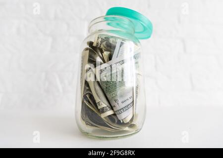 Faltet Geld in einem Glas auf einem weißen Holzhintergrund. Der Ort des Hintergrundbildes für Text. Stockfoto