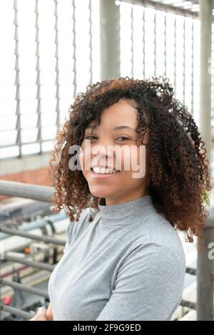 Junge schwarze Frau in grauem T-Shirt blickt auf lächelnde Kamera, während sie ihre Haare berührt. Stockfoto