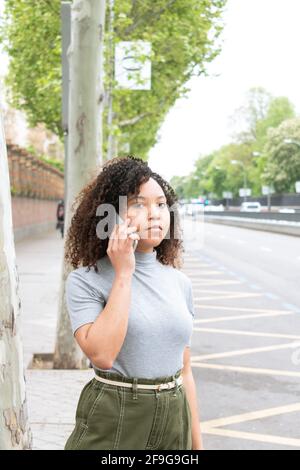 Schwarze Frau mit lockigem Haar ruft in der Stadt ein Taxi auf einem Handy. Stockfoto