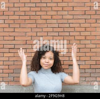 Junge schwarze Mädchen mit lockigen Haaren zeigt nach oben auf eine Kopie Platz mit einem roten Backstein Hintergrund. Stockfoto