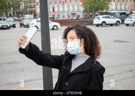 Junge schwarze Pendlerin nimmt ein Selfie, während sie eine Maske trägt und einen Rucksack trägt. Stockfoto