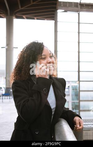 Lockiges Mädchen, das auf einem Handy spricht und dabei aus dem Rahmen schaut. Stockfoto