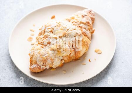 Mandelcroissant auf einem Teller, Nahaufnahme. Süßes französisches Gebäck gebackenes Croissant mit Mandelflocken und Puderzucker Stockfoto