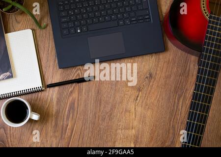 Rot-schwarze klassische Gitarre auf Holzboden, neben Computer, Telefon und Notebook-Stift Stockfoto