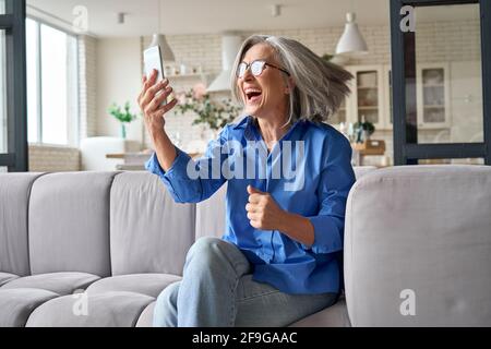 Überrascht verließ reife Frau im Alter von 60 Jahren zu Hause mit Handy. Stockfoto