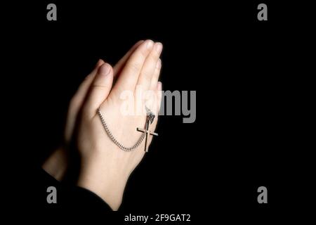 Betende Hände halten einen Rosenkranz, Closeup halten Halskette mit Kreuz, beten für gott im Dunkeln, religiöse christliche Symbol Stockfoto
