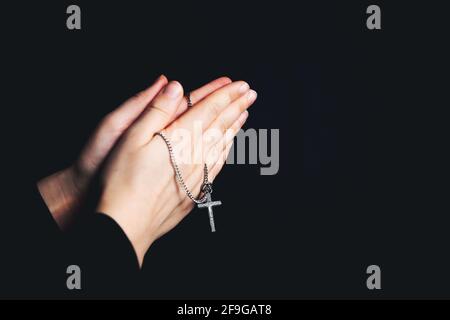 Betende Hände halten einen Rosenkranz, Closeup halten Halskette mit Kreuz, beten für gott im Dunkeln, religiöse christliche Symbol Stockfoto