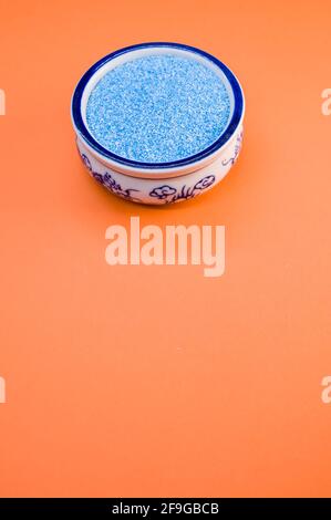 Eine vertikale Aufnahme von blauem Sand in einer porzellanschale Auf einer orangefarbenen Oberfläche Stockfoto