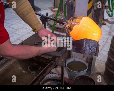 Handwerkliche Hände bilden das rote formbare Glas auf dem Glasbläserrohr. Traditionelle Glasformtechnik. Handgemachtes Glasstudio in Kunratice. Stockfoto