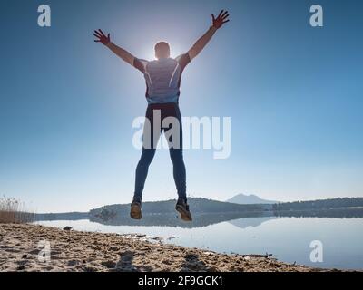 Mann, der bei Sonnenuntergang am Strand springt. Lustige glückliche Mann springt in der Luft mit aufgesetzt Arme Stockfoto