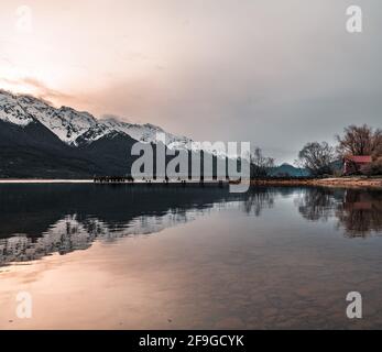 Ein atemberaubender Blick auf den Sonnenaufgang auf eine schneebedeckte Bergkette spiegelt sich wider Im Winter auf einem spiegelartigen, ruhigen See Stockfoto