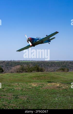 Kleine einzelne Propellermaschine fliegt tief über den Boden hügelige Landschaft mit grünem Gras und blauem Himmel an einem sonnigen Tag, niemand. Stockfoto