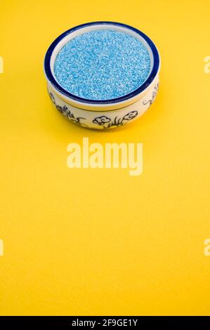 Eine vertikale Aufnahme von blauem Sand in einer porzellanschale Auf einer leuchtend gelben Oberfläche Stockfoto