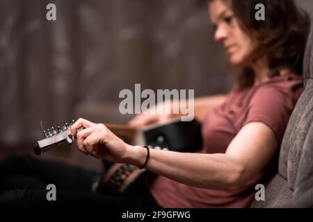 Frau, die Gitarre zu Hause auf der Couch stimmt Stockfoto