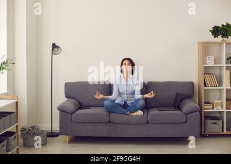 Frau mit geschlossenen Augen entspannt sich und meditiert in Lotushaltung Auf der Couch Stockfoto