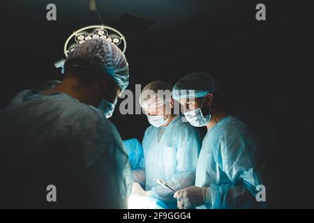 Ein internationales Ärzteteam führt eine komplexe chirurgische Operation an einem unter Anästhesie stehenden Patienten durch. Moderner Operationssaal und erfahrene Chirurgen Stockfoto