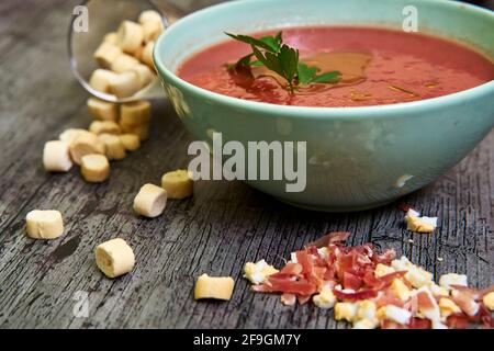 Nahaufnahme der andalusischen Gazpacho-Schüssel mit Petersilie und nativem Olivenöl extra, begleitet von Croutons, Serrano-Schinken und gehacktem gekochtem Ei. Concep Stockfoto