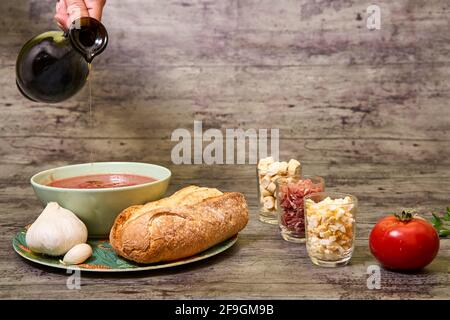Natives Olivenöl extra, das mit andalusischem Gazpacho in einer Schüssel serviert wird. Begleitet von Brot und Knoblauch, und auf der rechten Seite sind Croutons, Ei und Serran Stockfoto