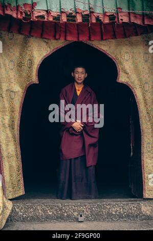 Ein junger Mönch in rotem Gewand steht am Eingang zum Kloster Samye, Lhasa, Autonome Region Tibet, China Stockfoto