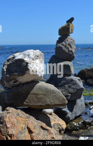 Felsbrocken an einem Strand in Fuengirola, Spanien - Kunst Felsenskulpturen aus vier oder fünf großen Steinen, aufgestellt gegen den blauen Himmel und das ruhige Meer. Stockfoto