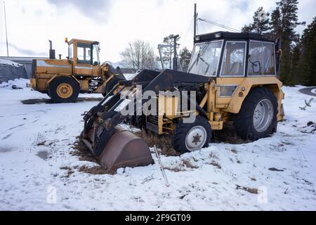 Zwei alte rostige Ladertraktoren stehen auf einem Schneefeld - klein und groß, Winterzeit. Stockfoto