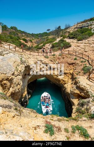 Ausflugsboot im türkisfarbenen Meer führt durch Felsenhöhlen und Felsbögen, Klippen aus Sandsteinfelsen, Algarve, Lagos, Portugal Stockfoto