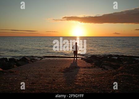 Heacham, Großbritannien. April 2021. Eine Person beobachtet den Sonnenuntergang vom Slipway in Heacham, Norfolk. Kredit: Paul Marriott/Alamy Live Nachrichten Stockfoto