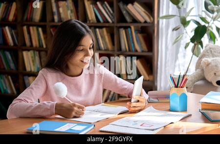 Glücklich lächelndes arabisches Schulmädchen mit Telefon für virtuelle Online-Studie zu Hause. Stockfoto