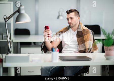 Im Büro erkrankt der Manager, bedeckt sich mit einer Decke und ruft den Arzt an, um die Symptome der Krankheit zu melden. Stockfoto