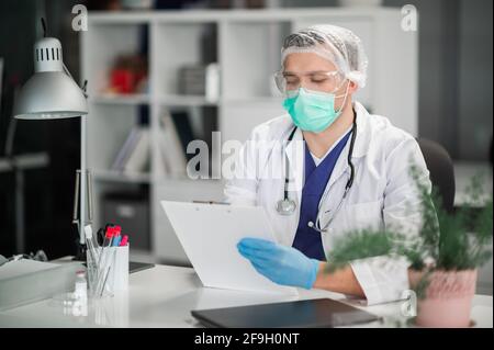 Ein erfahrener Therapeut schaut sich die Krankenakte des Patienten an der Rezeption in seinem Büro an. Stockfoto