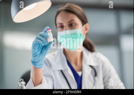 Eine junge Labortechnikerin mit medizinischer Maske zeigt in ihrem Labor im Krankenhaus einen Coronavirus-Impfstoff. Stockfoto