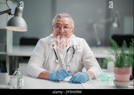 Ein Professor für medizinische Wissenschaften führt ein Praktikum in einem Krankenhaus durch, er sitzt an einem Tisch und schaut auf die Kamera. Stockfoto