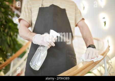 Kurzer Schuss eines nicht erkennbaren Mannes, der Treppengeländer desinfiziert und Möbel im Café reinigt, Kopierbereich Stockfoto