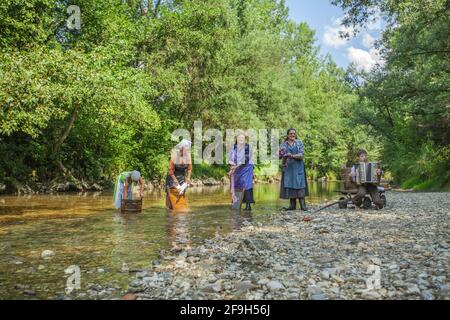 DOMZALE, SLOWENIEN - 30. Jun 2019: Alte Frauen in traditioneller Kleidung waschen schmutzige Kleidung am Fluss an sonnigen Tagen Stockfoto