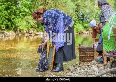 DOMZALE, SLOWENIEN - 30. Jun 2019: Alte Frauen in traditioneller Kleidung waschen schmutzige Kleidung am Fluss an sonnigen Tagen Stockfoto