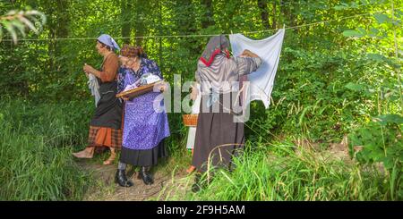 DOMZALE, SLOWENIEN - 30. Jun 2019: Alte Frauen in traditioneller Kleidung waschen schmutzige Kleidung am Fluss an sonnigen Tagen Stockfoto