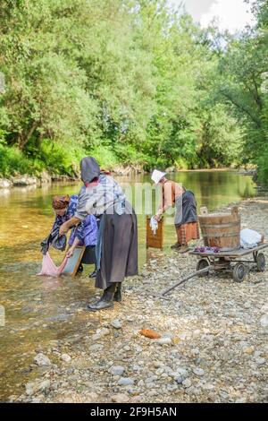 DOMZALE, SLOWENIEN - 30. Jun 2019: Alte Frauen in traditioneller Kleidung waschen schmutzige Kleidung am Fluss an sonnigen Tagen Stockfoto