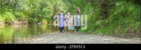 DOMZALE, SLOWENIEN - 30. Jun 2019: Alte Frauen in traditioneller Kleidung waschen schmutzige Kleidung am Fluss an sonnigen Tagen Stockfoto