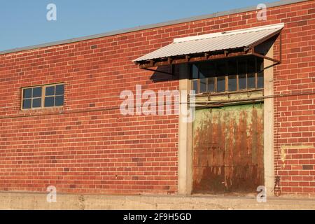 Die Farbe verblasst an der Laderampentür eines verlassenen roten Backsteingebäudes. Stockfoto