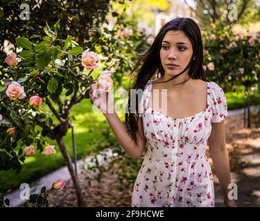 Schöne Latina Teen bewundern Rosen in einem Garten in lite Kleid für den Frühling Stockfoto