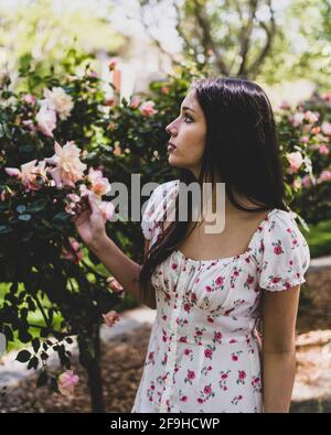 Schöne Latina Teen bewundern Rosen in einem Garten in lite Kleid für den Frühling Stockfoto